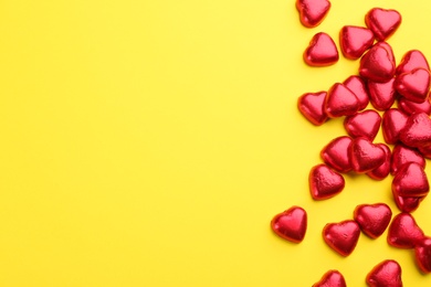 Photo of Heart shaped chocolate candies in red foil on yellow background, flat lay. Space for text