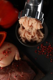 Photo of Electric meat grinder with chicken mince and products on black table, flat lay