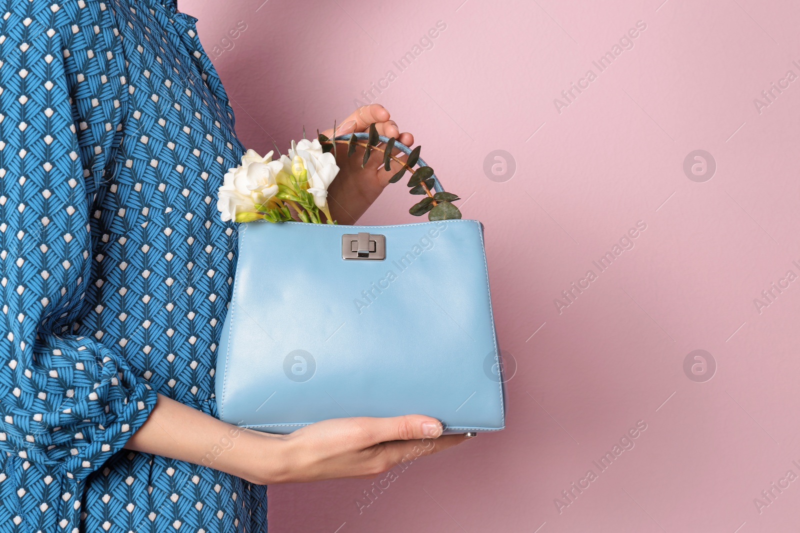 Photo of Stylish woman with handbag and spring flowers against color background, closeup. Space for text