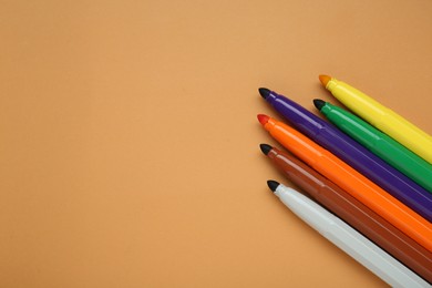 Different colorful markers on light brown background, flat lay. Space for text