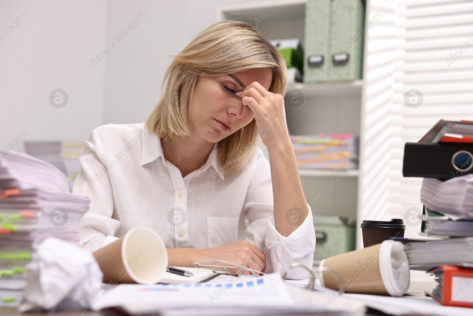 Photo of Overwhelmed woman surrounded by documents and paper coffee cups at workplace in office