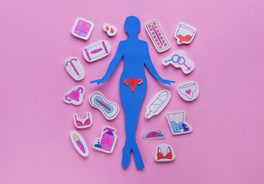 Photo of Woman`s health. Paper female figure and different stickers on pale pink background, flat lay