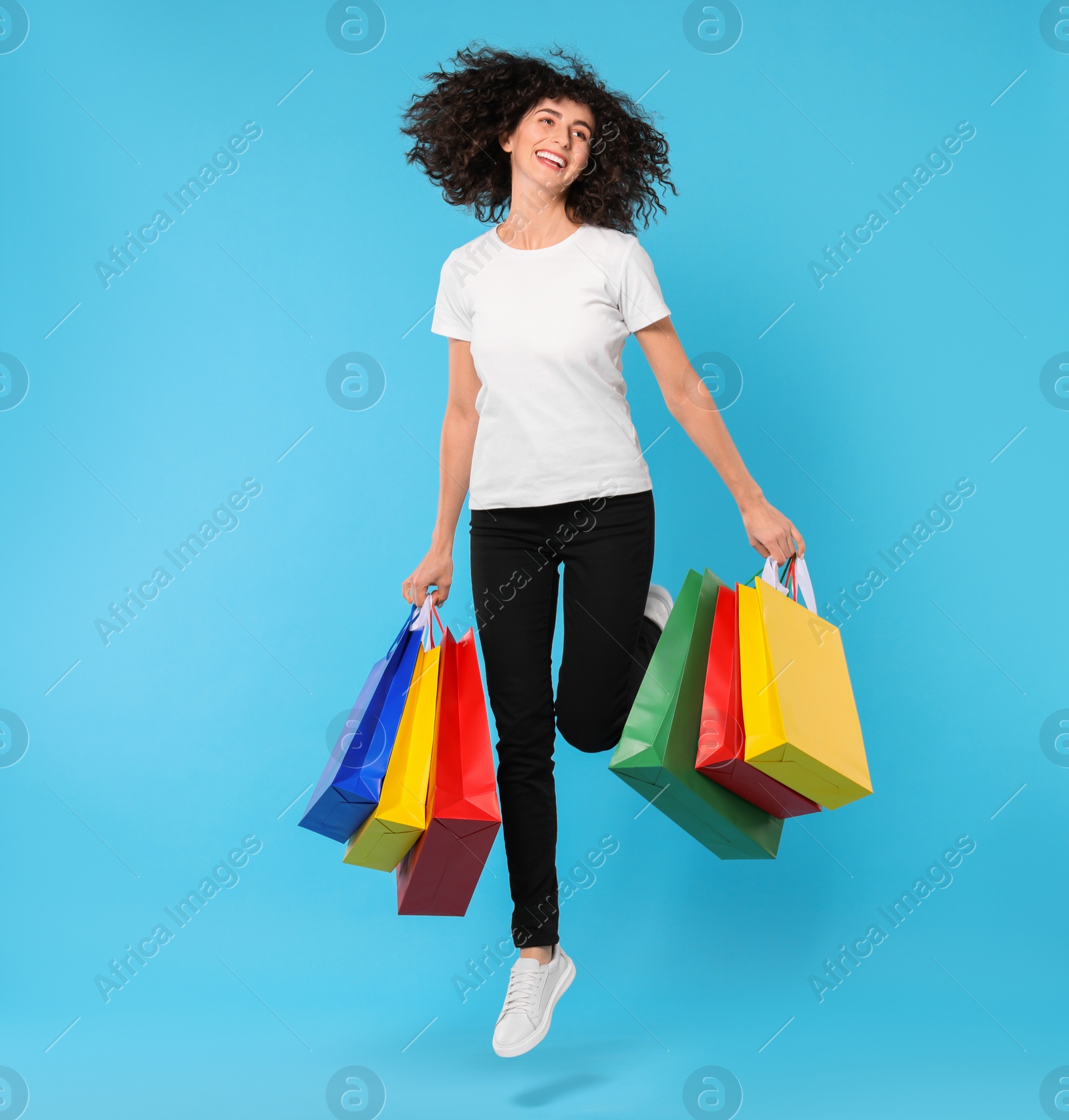 Photo of Happy young woman with shopping bags on light blue background