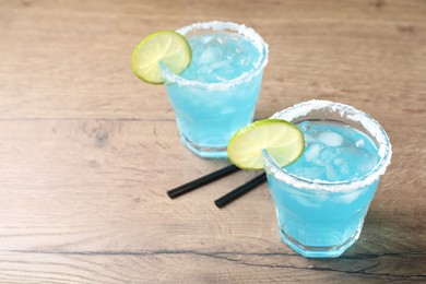 Refreshing light blue cocktail on wooden table, space for text