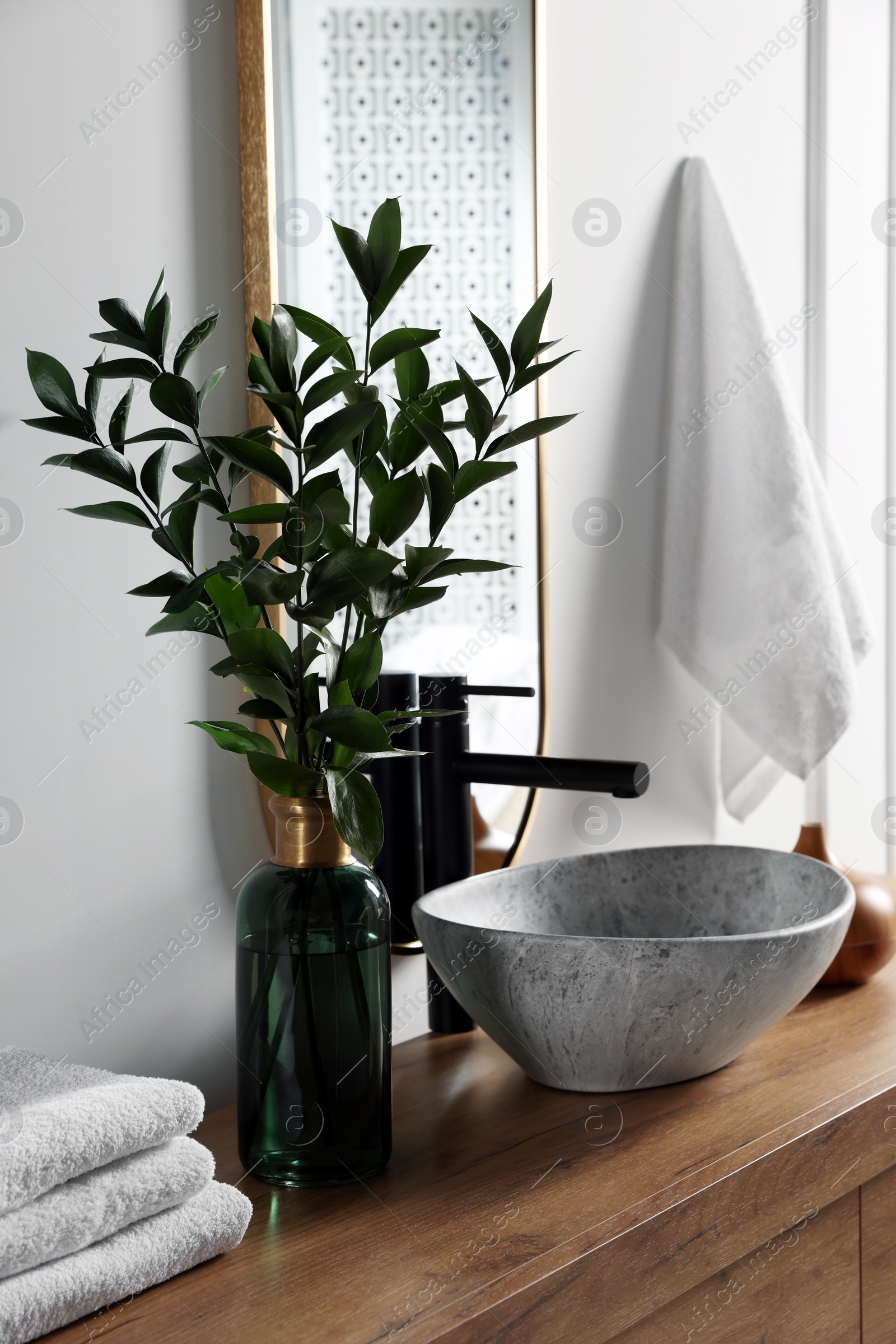 Photo of Eucalyptus branches and folded towels near stylish vessel sink on bathroom vanity. Interior design