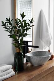 Photo of Eucalyptus branches and folded towels near stylish vessel sink on bathroom vanity. Interior design