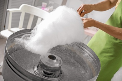 Woman making cotton candy using modern machine indoors, closeup