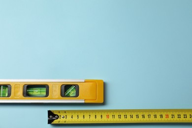 Photo of Building level and tape measure on light blue background, top view. Space for text