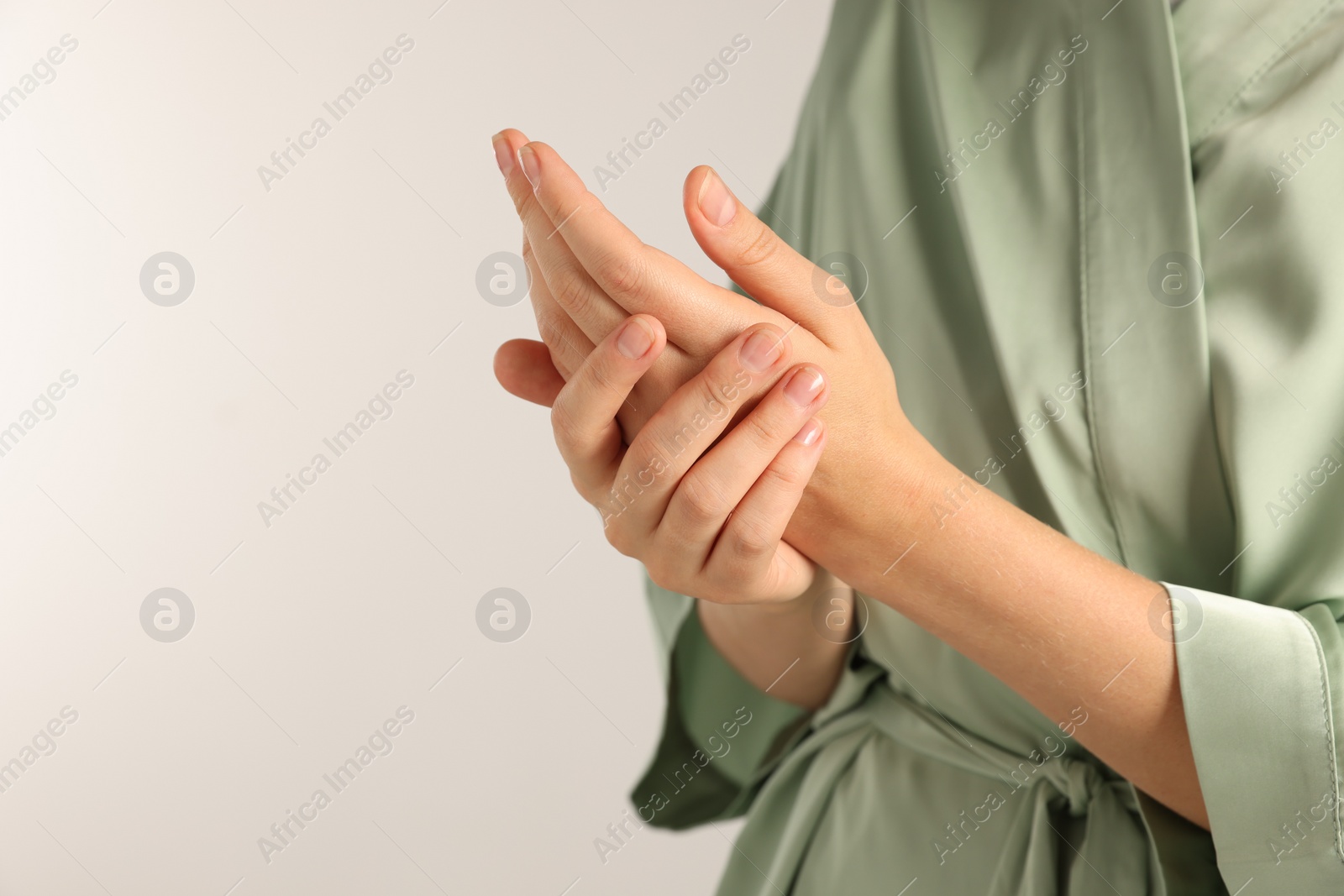 Photo of Woman applying cosmetic cream onto hand on light grey background, closeup. Space for text