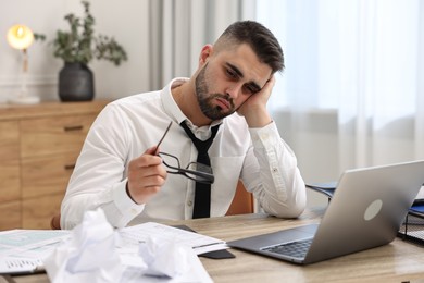 Overwhelmed man sitting at table with laptop and documents in office