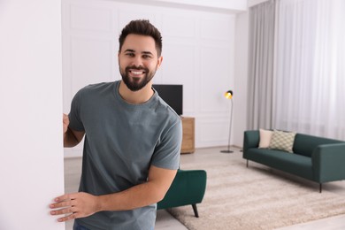 Happy man standing near white wall at home, space for text. Invitation to come in room