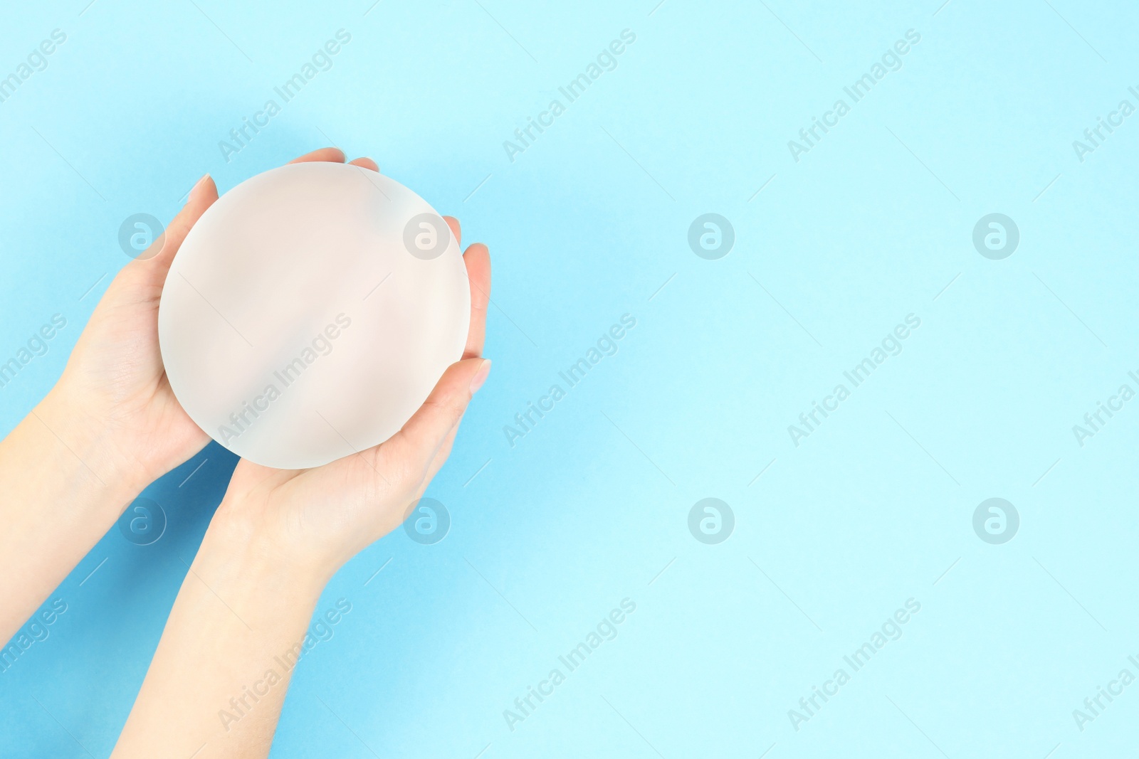 Photo of Woman holding silicone implant for breast augmentation on color background, top view with space for text. Cosmetic surgery