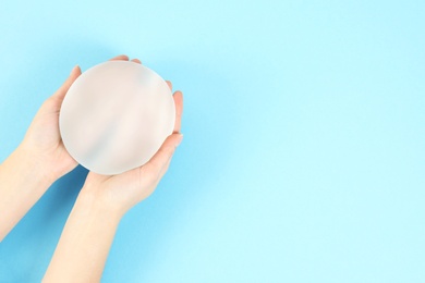 Photo of Woman holding silicone implant for breast augmentation on color background, top view with space for text. Cosmetic surgery