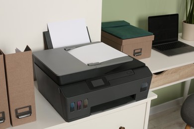 Photo of Modern printer with paper on white chest of drawers indoors