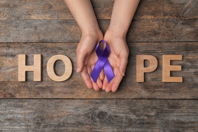 Photo of Woman with purple awareness ribbon and word HOPE on wooden background, top view