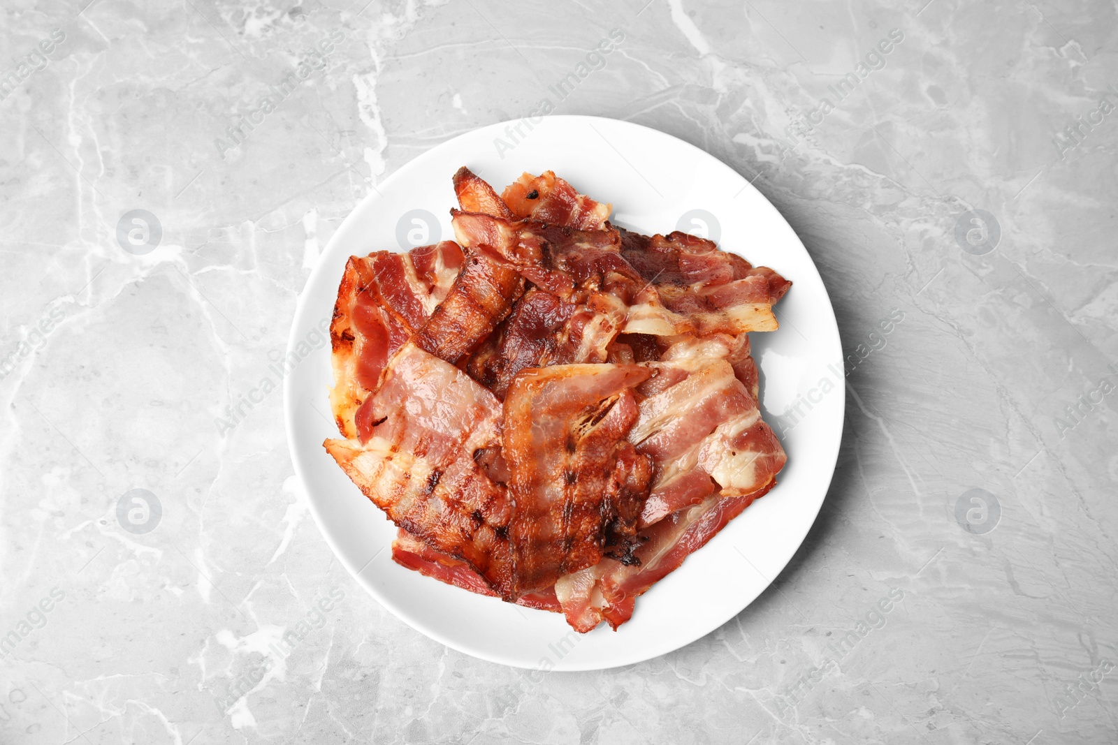 Photo of Slices of tasty fried bacon on light marble table, top view