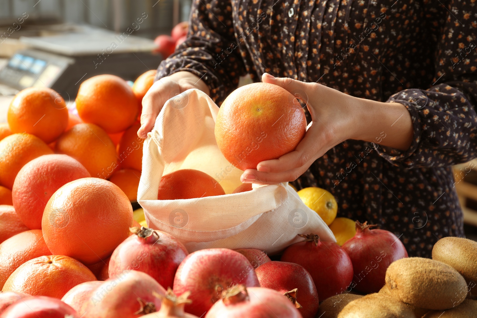 Photo of Woman putting orange into cotton eco bag at wholesale market, closeup. Life without plastic