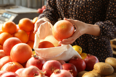 Woman putting orange into cotton eco bag at wholesale market, closeup. Life without plastic