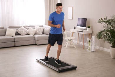 Photo of Sporty man training on walking treadmill at home