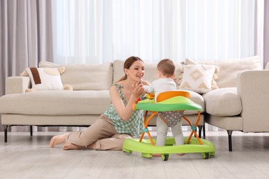 Cute boy making first steps with baby walker. Happy mother and her little son spending time together at home