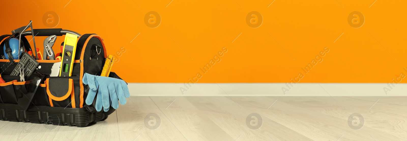 Image of Bag with different tools for repair on floor near orange wall, space for text. Banner design