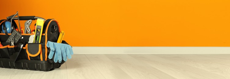 Bag with different tools for repair on floor near orange wall, space for text. Banner design