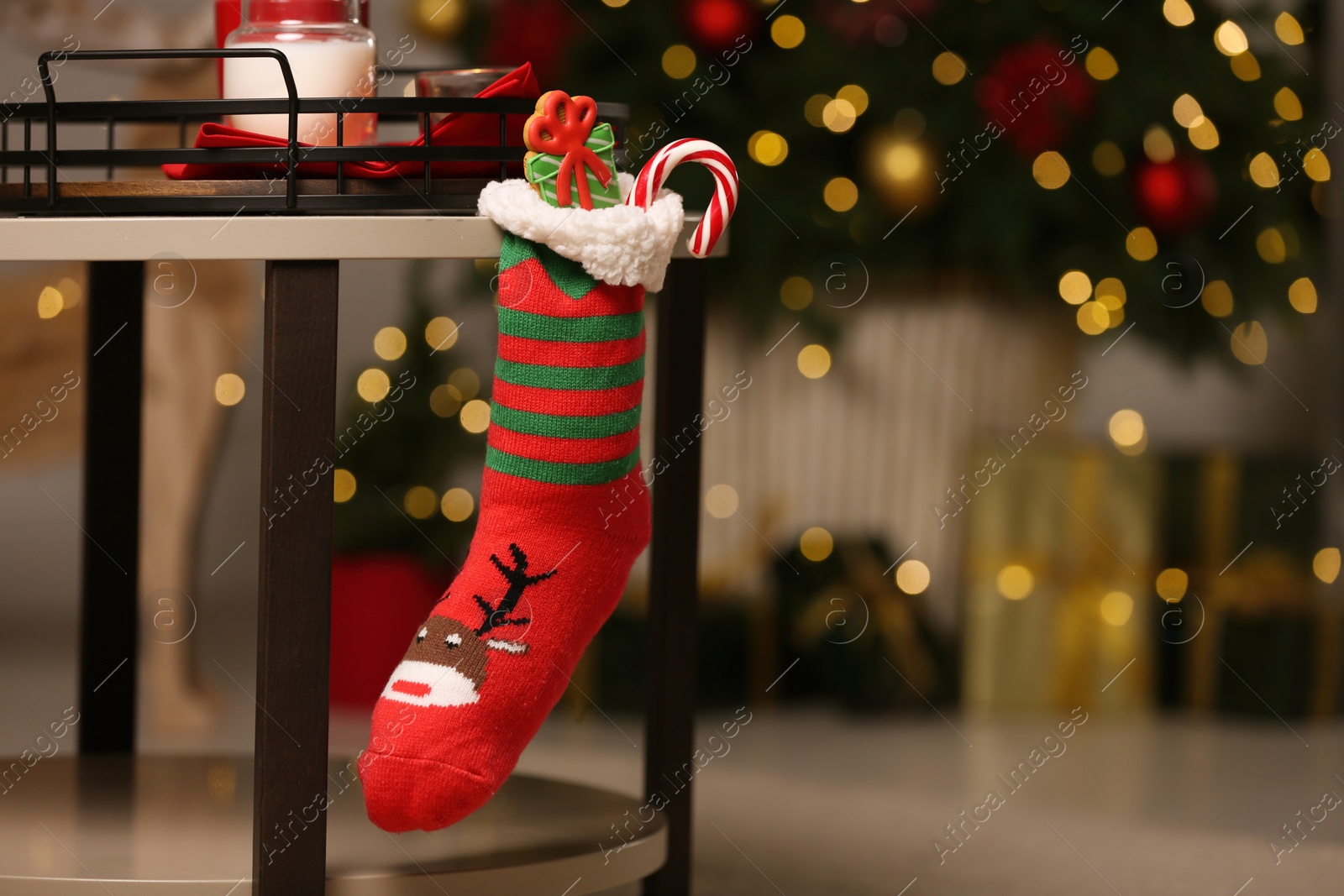 Photo of Stocking with presents hanging on table against blurred festive lights, space for text. Saint Nicholas Day tradition