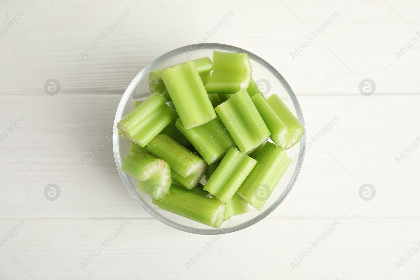 Photo of Cut celery in glass bowl on white wooden table, top view