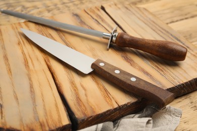 Photo of Sharpening steel and knife on wooden table, closeup