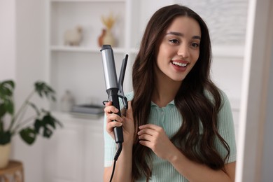Photo of Happy woman with curling hair iron at home