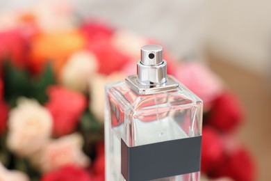 Bottle of perfume against bouquet of beautiful roses, closeup