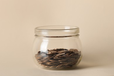 Photo of Glass jar with coins on beige background, closeup