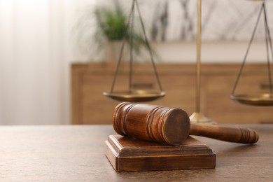 Photo of Wooden gavel, sound block and scales on table indoors, closeup. Space for text