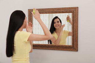 Photo of Woman applying dry shampoo onto her hair near mirror