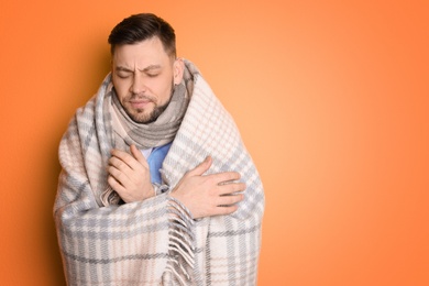 Mature man wrapped in blanket suffering from cold on color background
