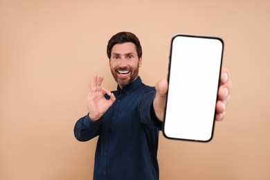 Handsome man showing smartphone in hand and OK gesture on light brown background