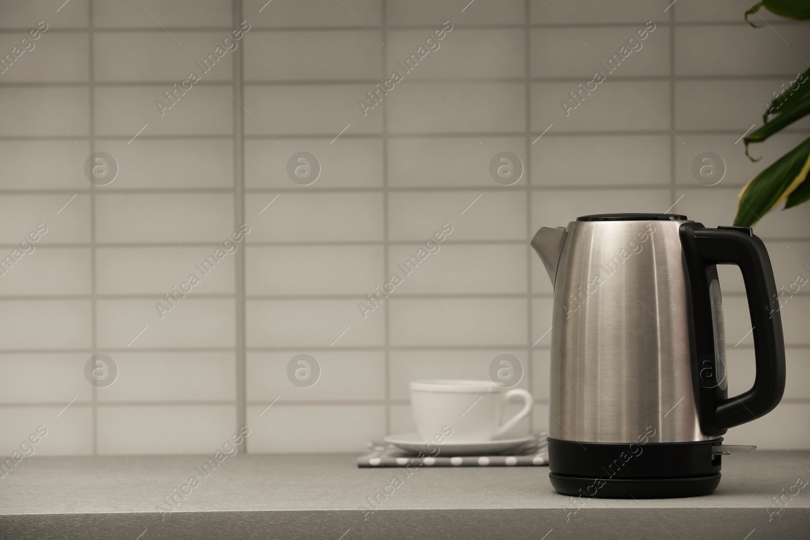 Photo of Modern electric kettle and cup on grey kitchen counter. Space for text