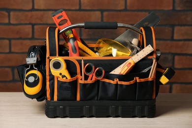 Photo of Bag with different tools for repair on white wooden table near brick wall