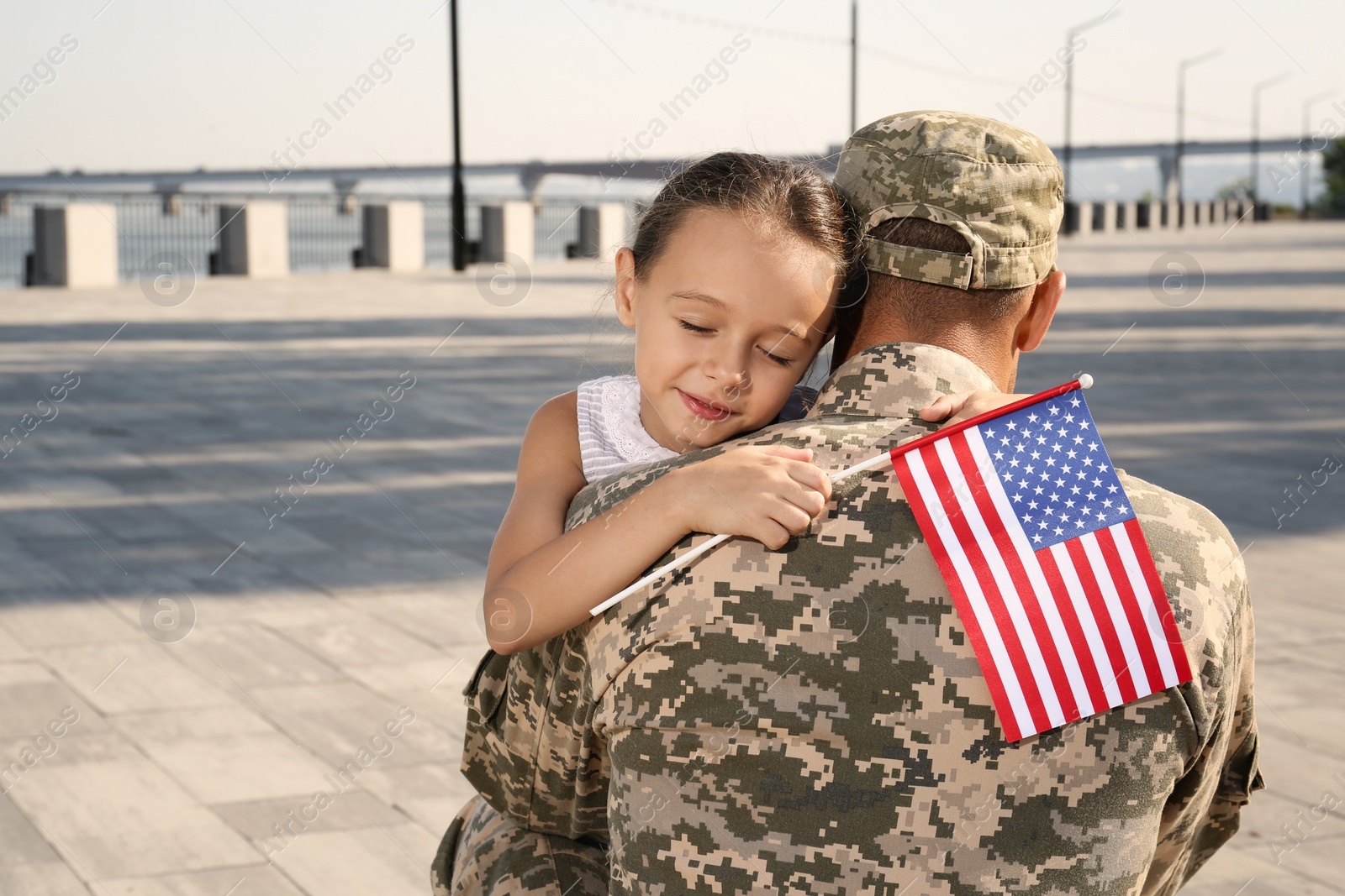 Photo of Soldier and his little daughter with flag of USA hugging outdoors, space for text