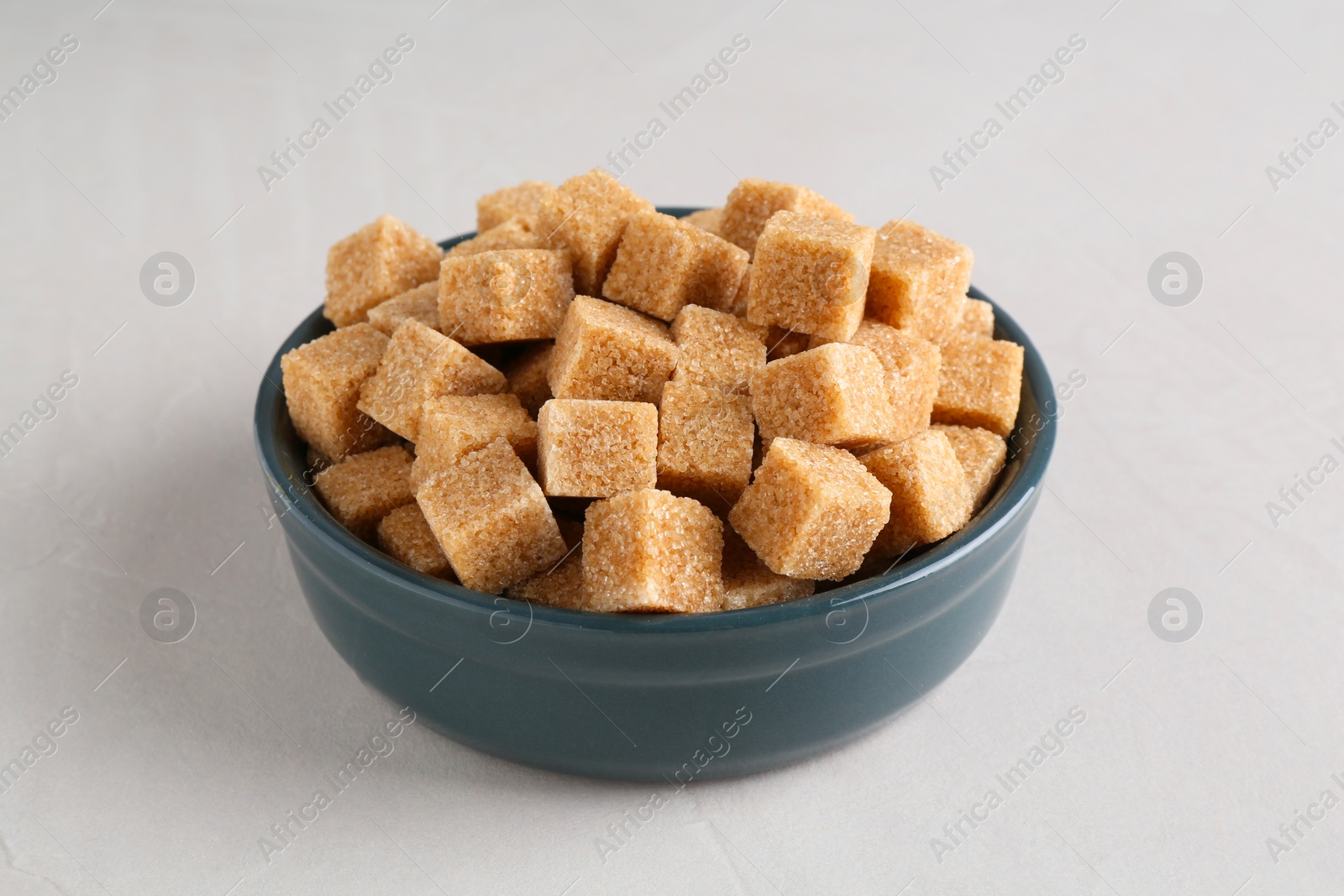 Photo of Brown sugar cubes in bowl on light textured table