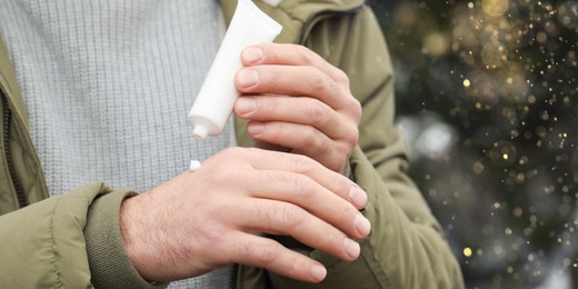Image of Man applying cream from tube onto hand outdoors, closeup. Winter care. Banner design