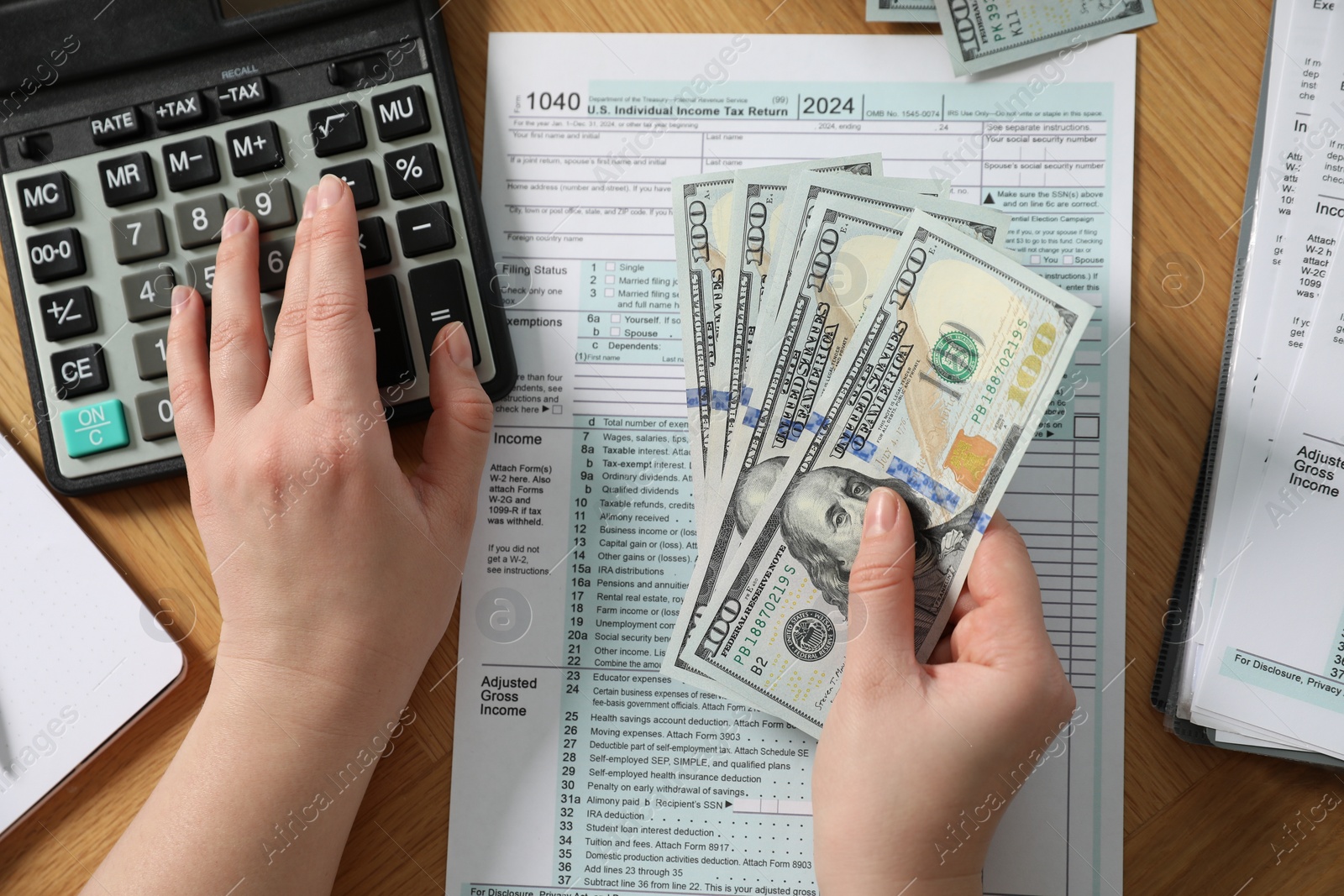 Photo of Payroll. Woman with dollar banknotes and calculator planning budget at wooden table, top view