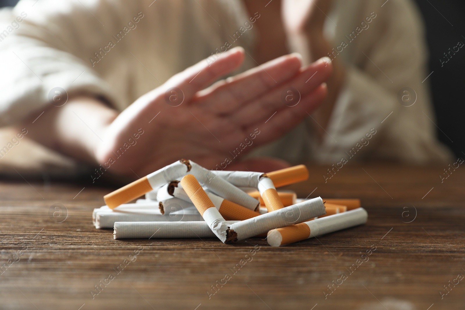 Photo of Stop smoking. Woman making stop gesture at wooden table, focus on whole and broken cigarettes