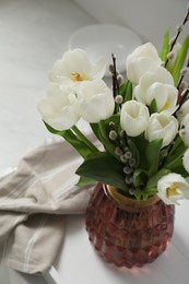 Beautiful bouquet of willow branches and tulips in vase on white table, above view