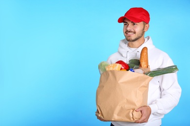 Photo of Food delivery courier holding paper bag with products on color background. Space for text