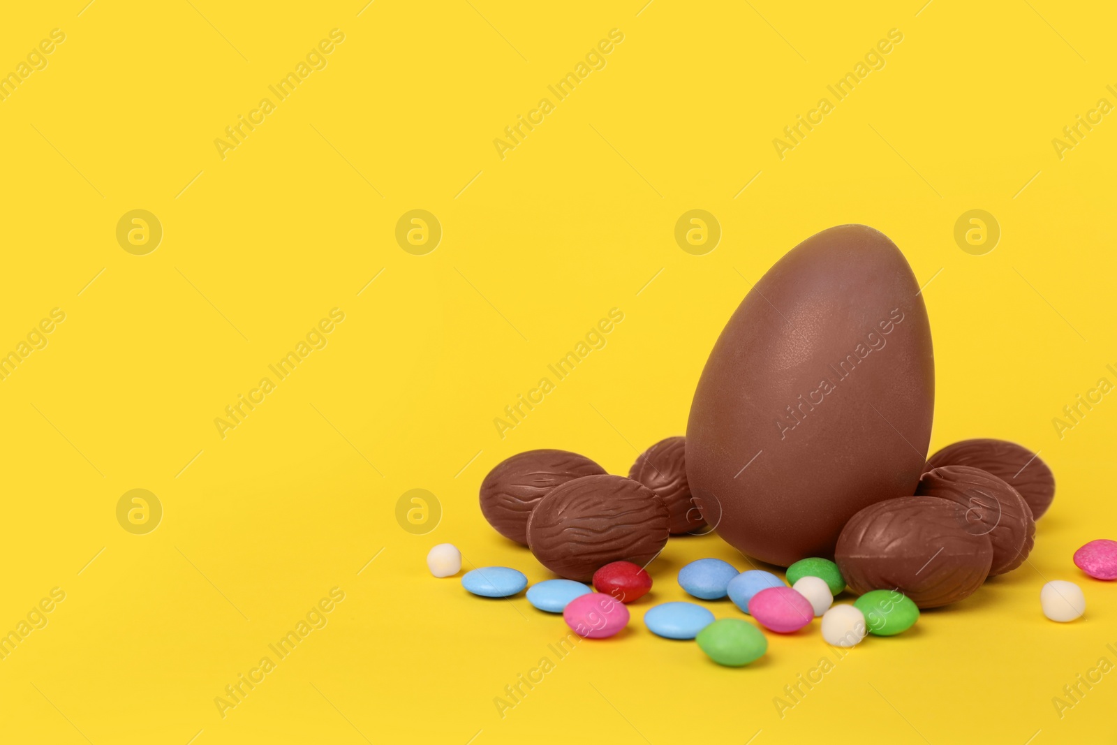 Photo of Delicious chocolate eggs and colorful candies on yellow background. Space for text