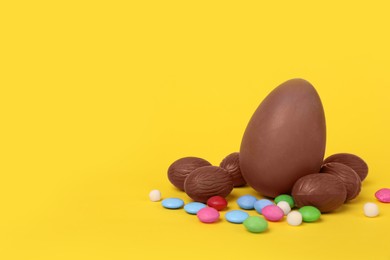 Photo of Delicious chocolate eggs and colorful candies on yellow background. Space for text
