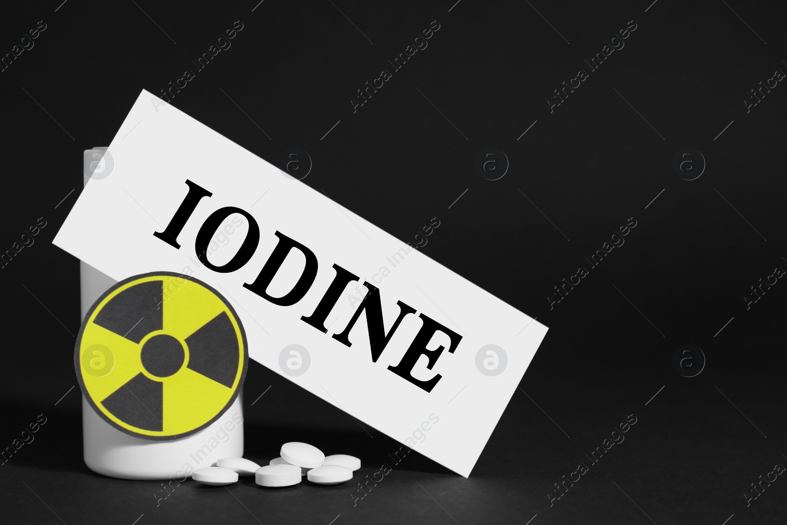 Photo of Paper note with word Iodine, bottle, pills and radiation sign on black background. Space for text