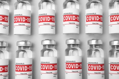 Glass vials with COVID-19 vaccine on light grey background, flat lay