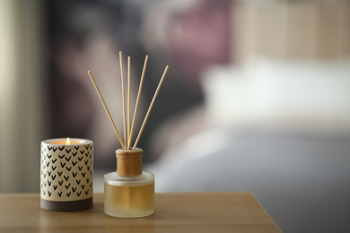 Aromatic reed air freshener and scented candle on table indoors. Space for text